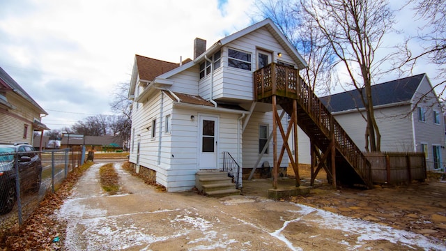 rear view of property featuring concrete driveway, a chimney, entry steps, and fence