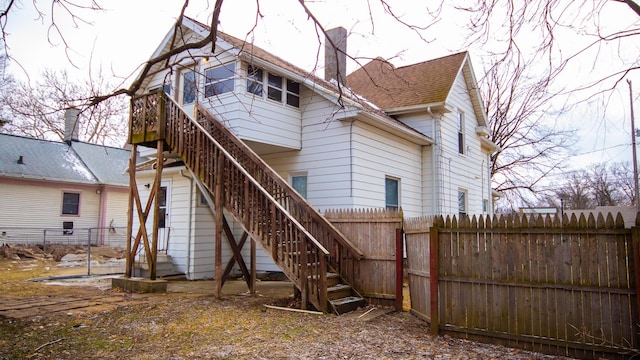 back of property featuring a shingled roof, a chimney, stairs, and fence