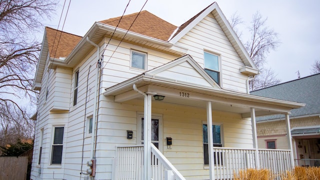 view of front facade featuring a porch, roof with shingles, and fence