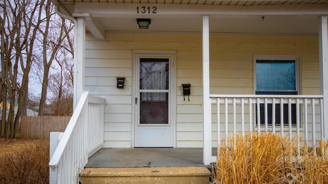 doorway to property with a porch and fence