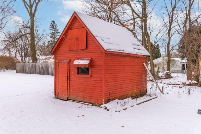 snow covered structure featuring an outbuilding and fence