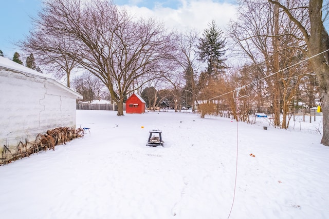 yard layered in snow featuring an outbuilding, a storage unit, and fence