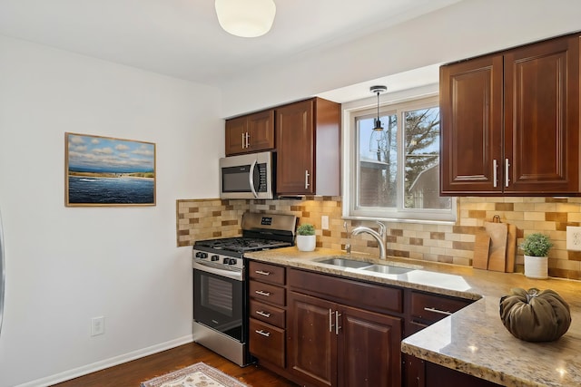 kitchen with light stone countertops, baseboards, a sink, appliances with stainless steel finishes, and backsplash