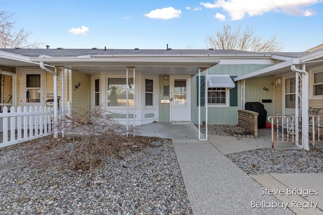 view of exterior entry with a porch, board and batten siding, and fence