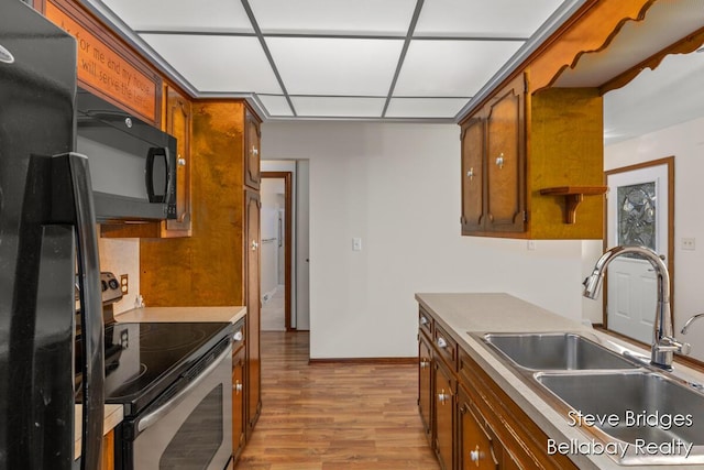 kitchen featuring light wood finished floors, brown cabinets, black appliances, a paneled ceiling, and a sink