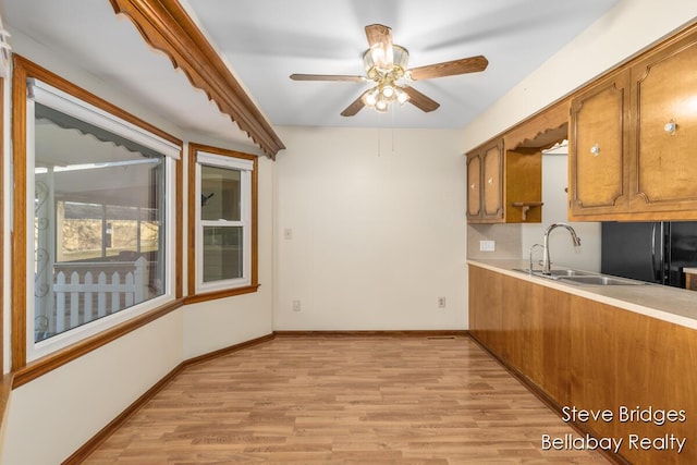 kitchen featuring brown cabinetry, light wood-style floors, freestanding refrigerator, and a sink