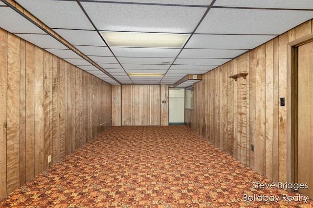 interior space with wooden walls, carpet, and a drop ceiling