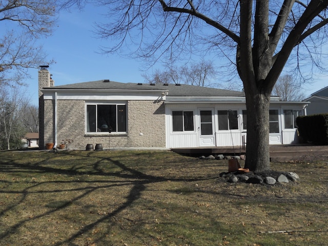 view of front of house with roof with shingles, a sunroom, a chimney, a front lawn, and brick siding