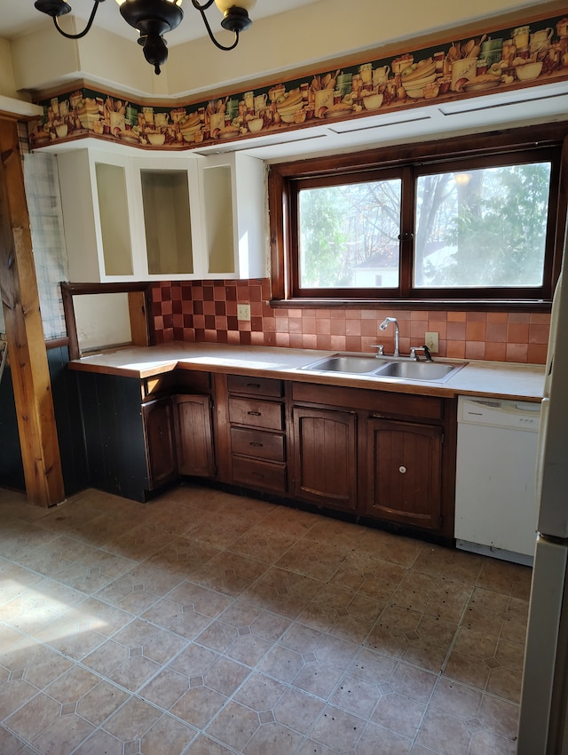 kitchen with white dishwasher, light countertops, a sink, and tasteful backsplash