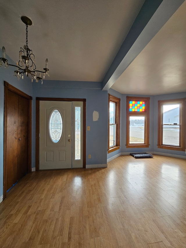 entryway with plenty of natural light, baseboards, light wood-style floors, and a notable chandelier