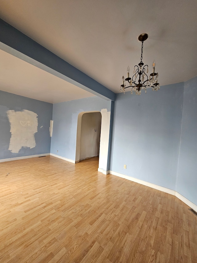 unfurnished room featuring light wood-type flooring, baseboards, arched walkways, and a notable chandelier