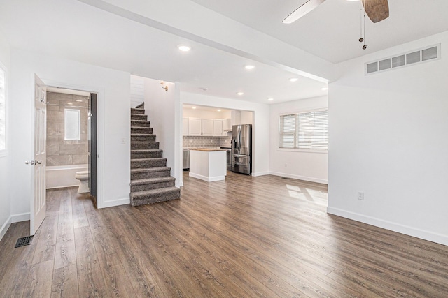 unfurnished living room with visible vents, dark wood-type flooring, ceiling fan, baseboards, and stairway