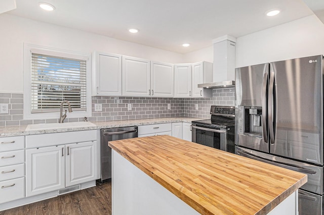 kitchen featuring visible vents, a sink, wood counters, stainless steel appliances, and wall chimney range hood