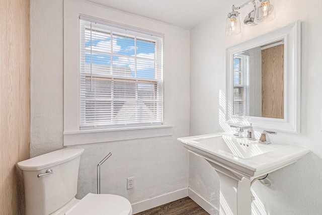 half bath featuring toilet, wood finished floors, baseboards, and a sink