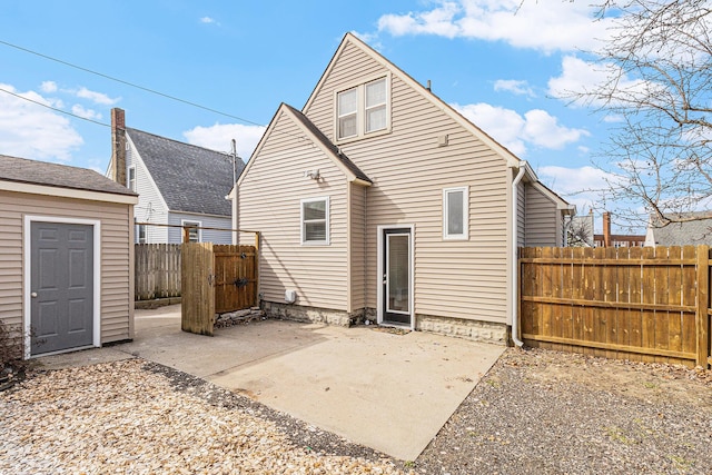 rear view of property featuring an outdoor structure, a patio, and fence