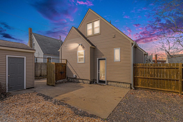 back of property at dusk with a patio area, an outdoor structure, and fence