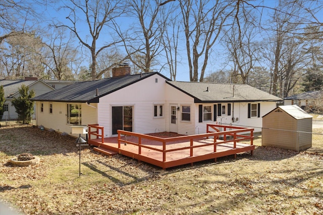 rear view of property featuring a fire pit, a wooden deck, a chimney, a storage shed, and an outdoor structure