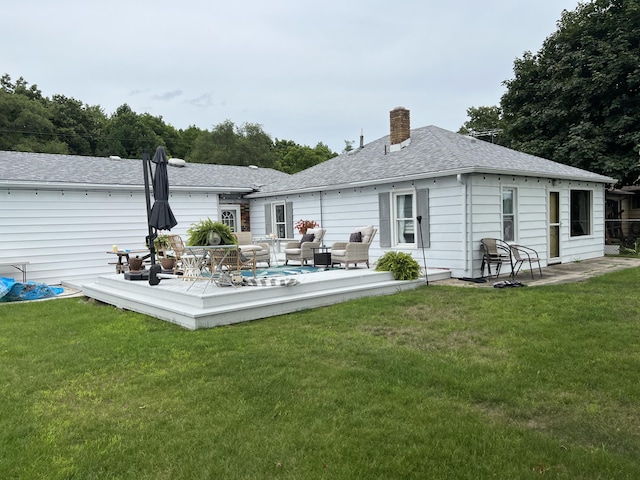 rear view of house with a lawn, a deck, a chimney, and a shingled roof