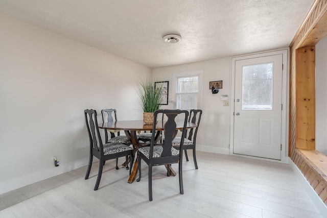 dining space featuring baseboards, light wood finished floors, and a textured ceiling