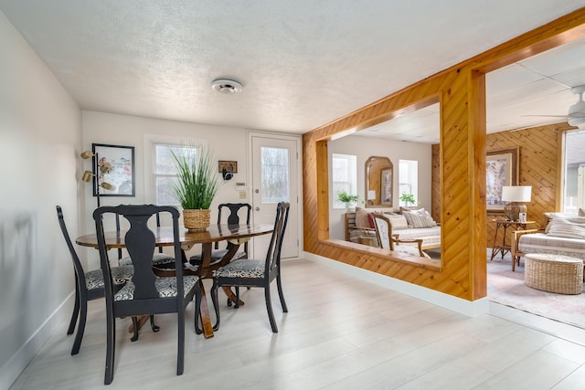 dining space with light wood-style flooring, a healthy amount of sunlight, wood walls, and a textured ceiling