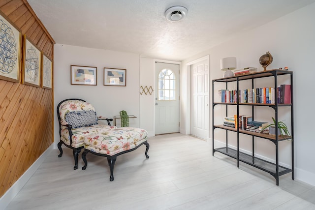 sitting room with wooden walls, a textured ceiling, baseboards, and wood finished floors