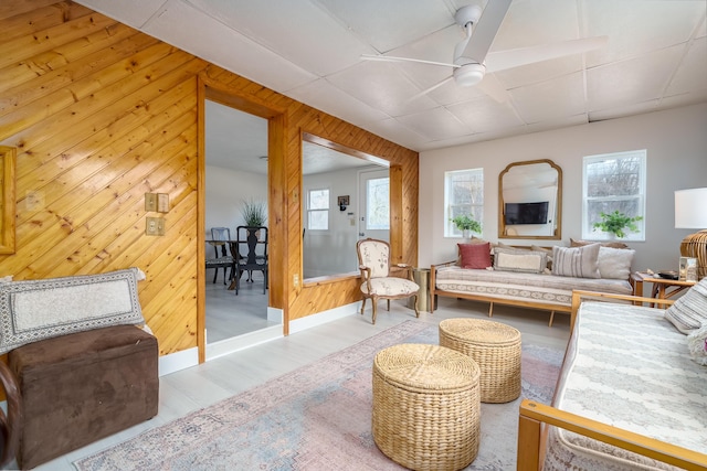 living area with wooden walls, baseboards, ceiling fan, a drop ceiling, and wood finished floors