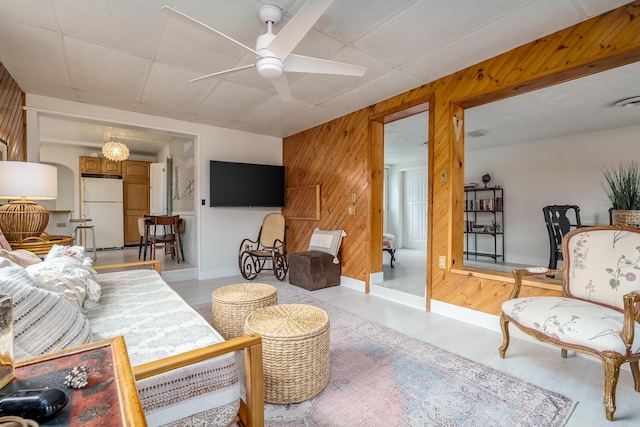 living area featuring a paneled ceiling, wooden walls, and a ceiling fan