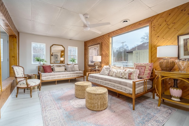 living room featuring a ceiling fan, visible vents, arched walkways, light wood-style floors, and wood walls