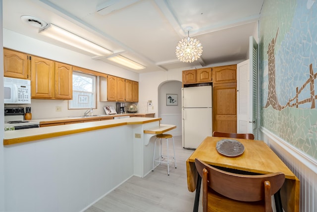 kitchen with white appliances, light wood finished floors, arched walkways, a sink, and light countertops