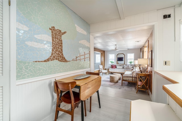 dining space featuring wallpapered walls, a ceiling fan, light wood-type flooring, and wainscoting