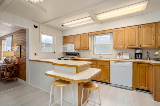 kitchen featuring white appliances, a peninsula, a sink, light countertops, and a kitchen bar