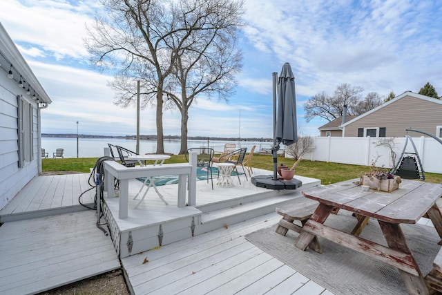 wooden deck with outdoor dining area, fence, and a water view