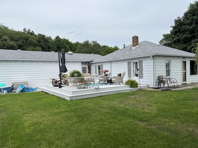 rear view of property with a lawn, a deck, a chimney, and a shingled roof