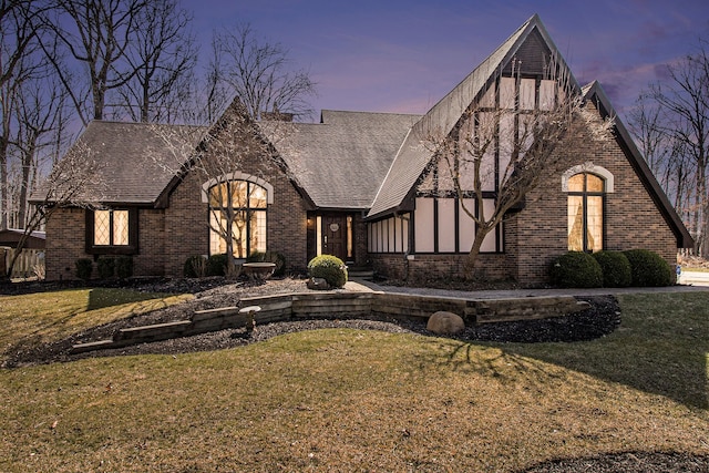 tudor house with brick siding, a front lawn, and a shingled roof