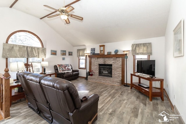 living room featuring a brick fireplace, wood finished floors, baseboards, and ceiling fan