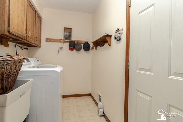 laundry area featuring a sink, washing machine and dryer, cabinet space, baseboards, and light floors