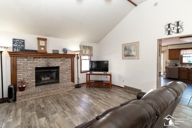 living area featuring a fireplace, wood finished floors, visible vents, and high vaulted ceiling