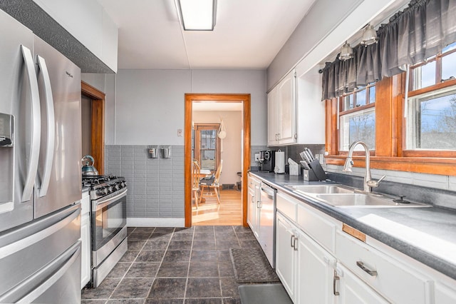 kitchen with tile walls, wainscoting, white cabinets, stainless steel appliances, and a sink