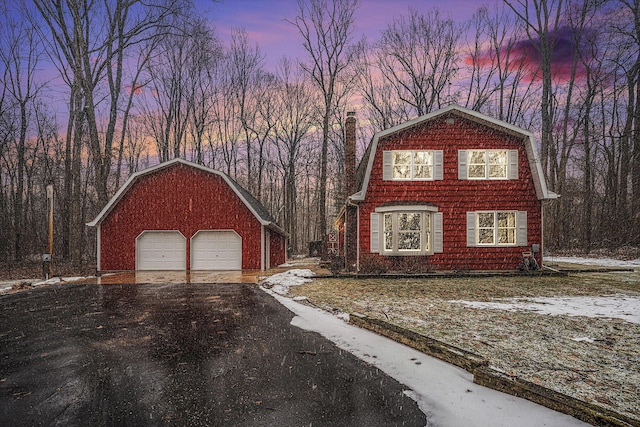 view of front of property with a gambrel roof, driveway, a detached garage, an outdoor structure, and a chimney