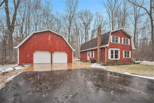 view of front facade with a gambrel roof, an outbuilding, roof with shingles, a garage, and a chimney