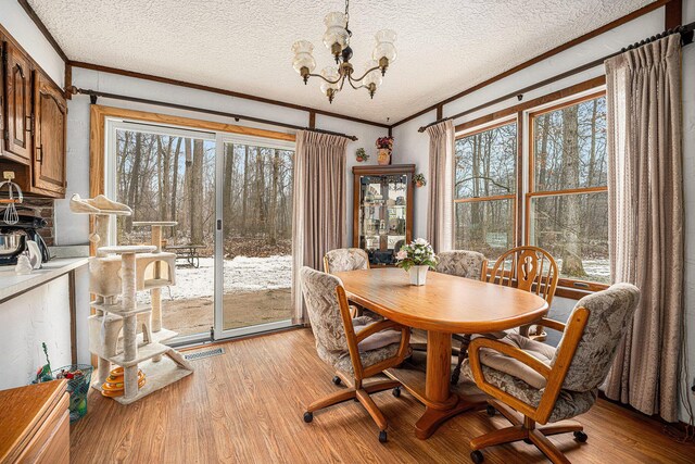 dining room featuring visible vents, light wood-style flooring, ornamental molding, a textured ceiling, and an inviting chandelier