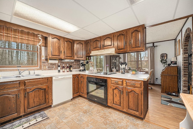 kitchen featuring under cabinet range hood, brown cabinets, black appliances, and a sink