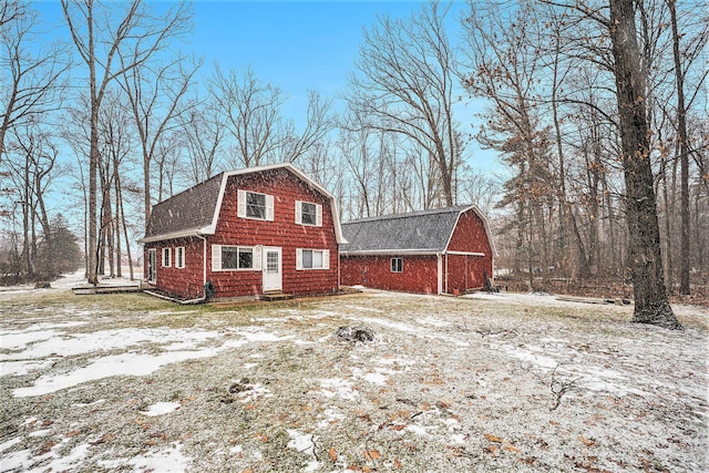 view of front facade featuring a barn, a gambrel roof, an outdoor structure, and a shingled roof