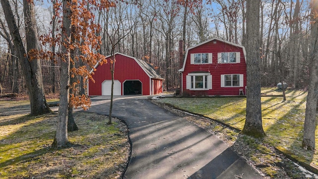 view of front facade with a barn, aphalt driveway, a gambrel roof, a garage, and an outbuilding