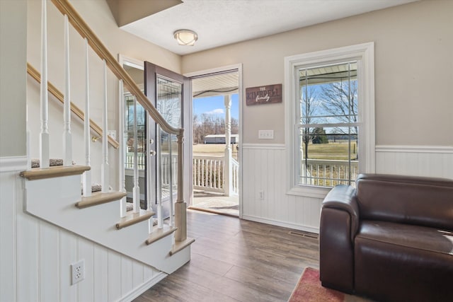 entrance foyer with stairs, wood finished floors, a wainscoted wall, and a wealth of natural light