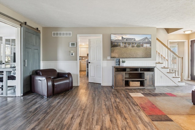 living area with visible vents, a barn door, dark wood-style floors, and a wainscoted wall