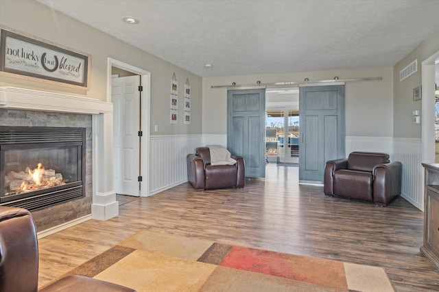 living area featuring visible vents, a premium fireplace, wainscoting, wood finished floors, and a textured ceiling