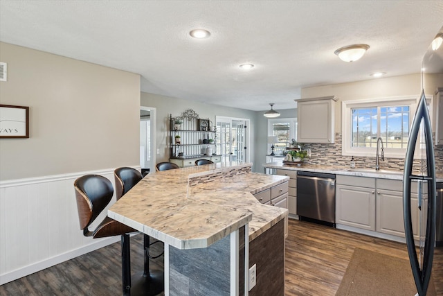 kitchen with a kitchen bar, stainless steel dishwasher, a center island, light countertops, and dark wood-style flooring