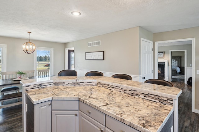 kitchen featuring visible vents, a center island, dark wood-type flooring, hanging light fixtures, and a notable chandelier