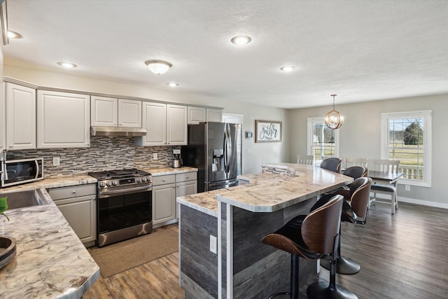 kitchen featuring a kitchen bar, under cabinet range hood, backsplash, stainless steel appliances, and light countertops